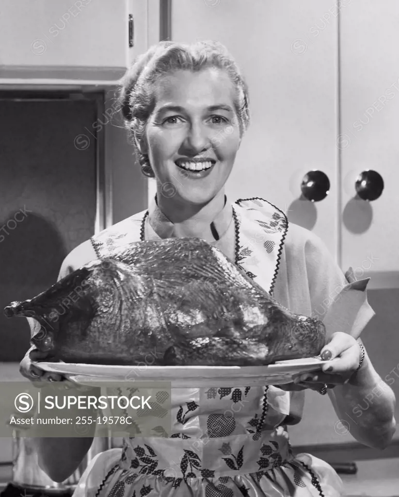 Mid adult woman holding a roast turkey and smiling