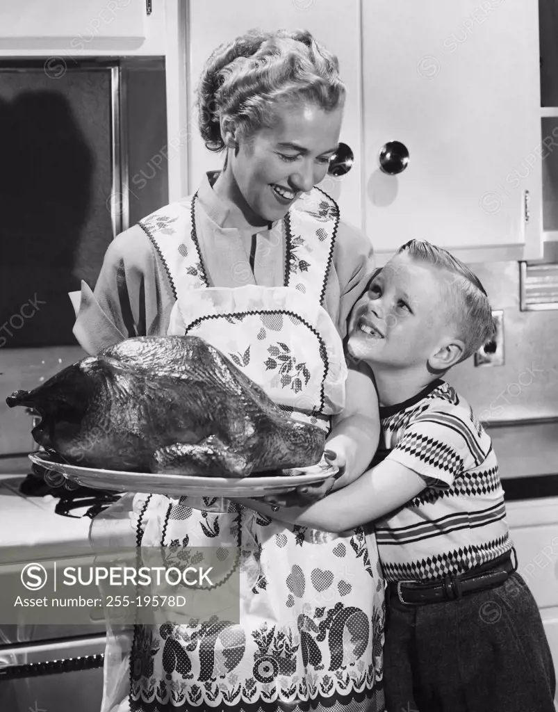 Mid adult woman holding a roast turkey with her son hugging her