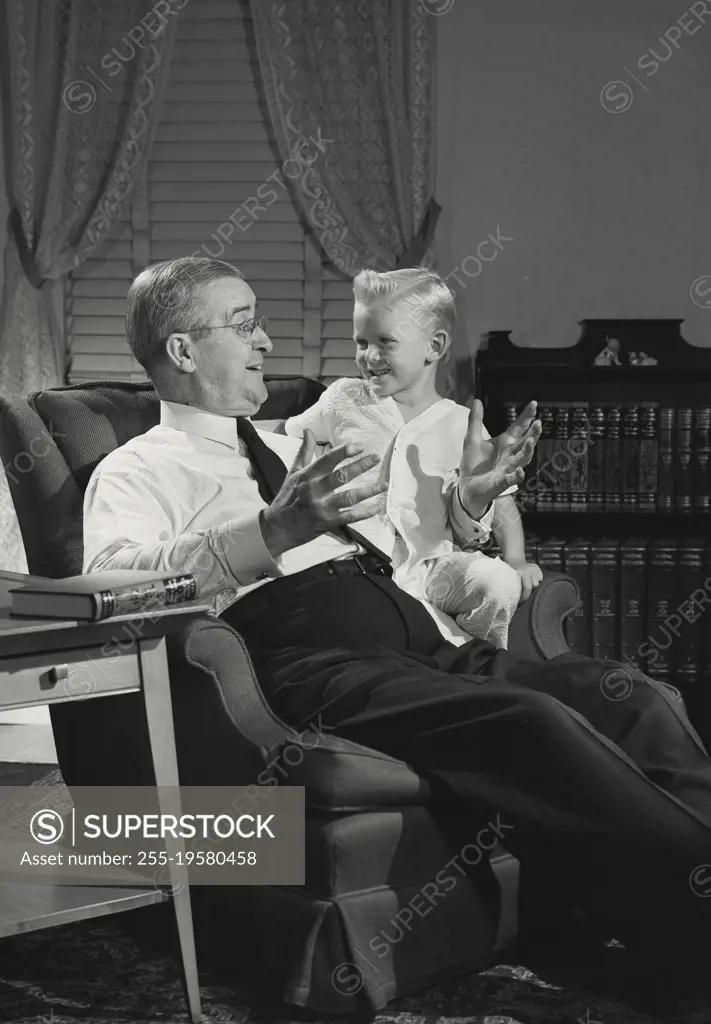 Vintage photograph. Man telling story to young boy on his lap