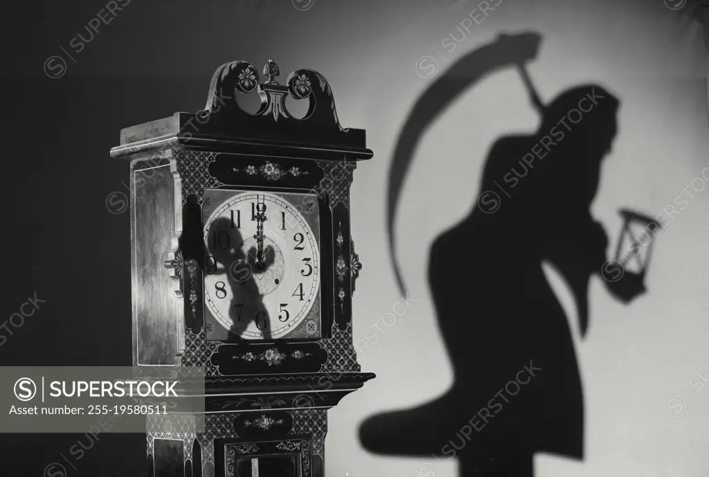 Vintage photograph. Grandfather Clock with shadow of baby casted on face and shadow of grim reaper in background