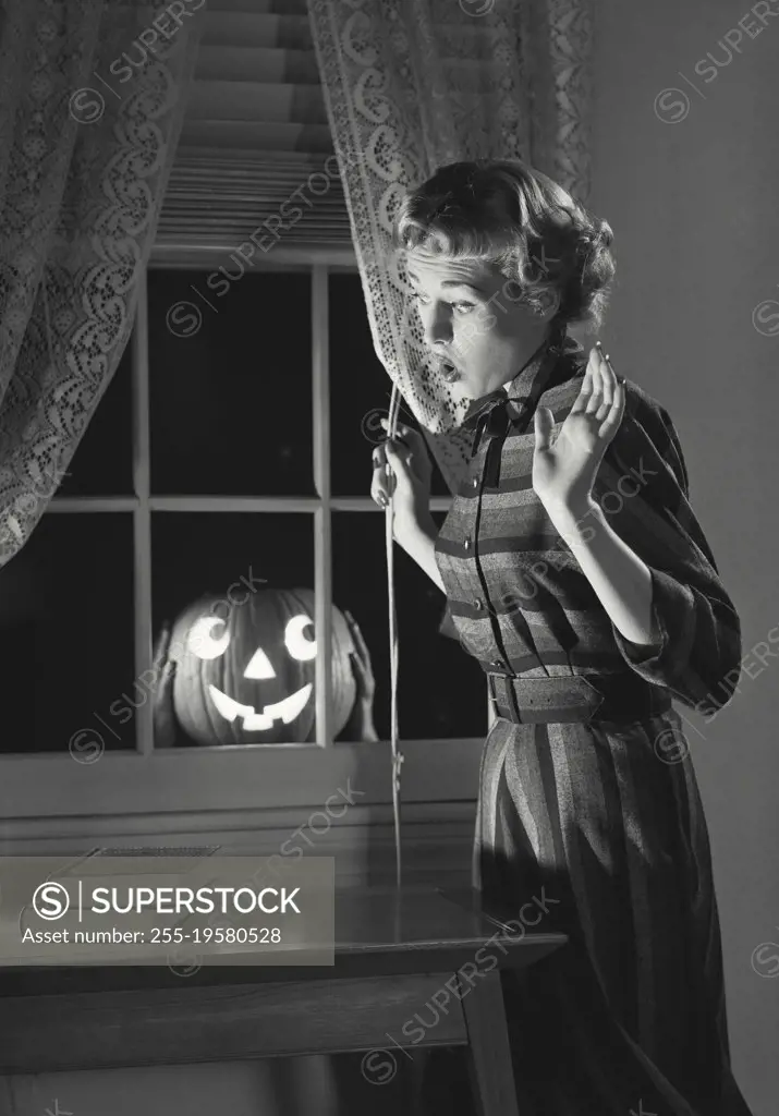 Vintage photograph. Woman scared of Jack o' Lantern in window