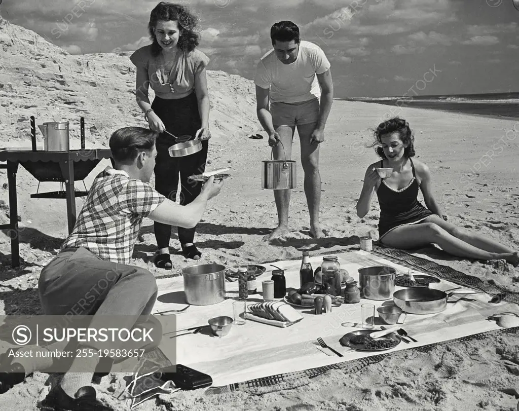 Vintage photograph. Two men and two women cooking on grill for picnic at the beach