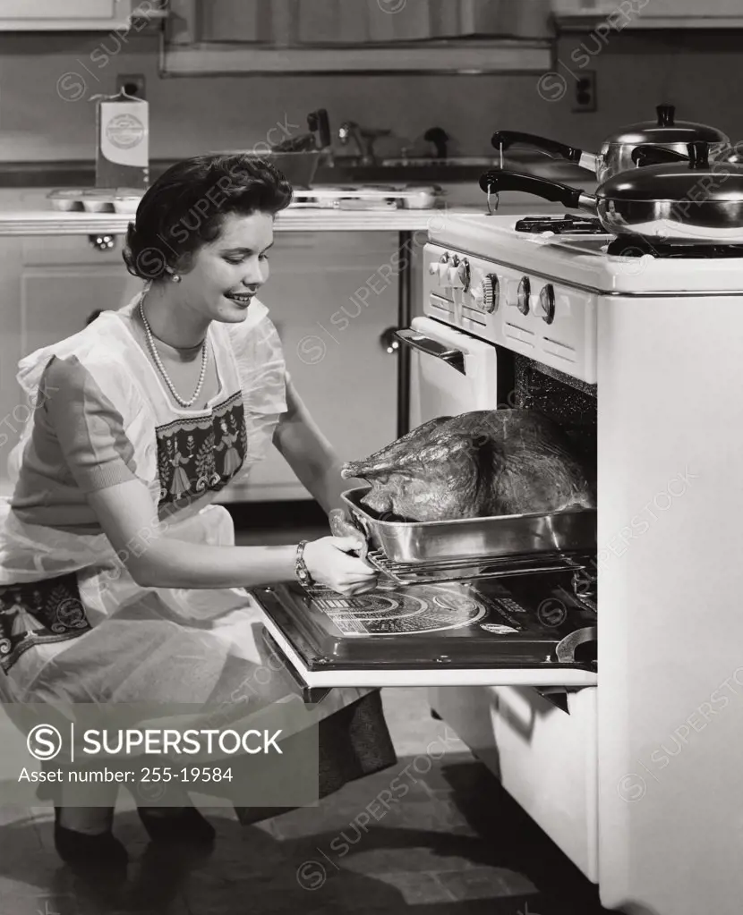 Side profile of a mid adult woman putting a turkey into an oven