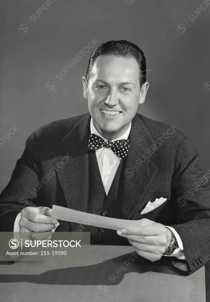 Vintage Photograph. Businessman in suit and bowtie holding up document