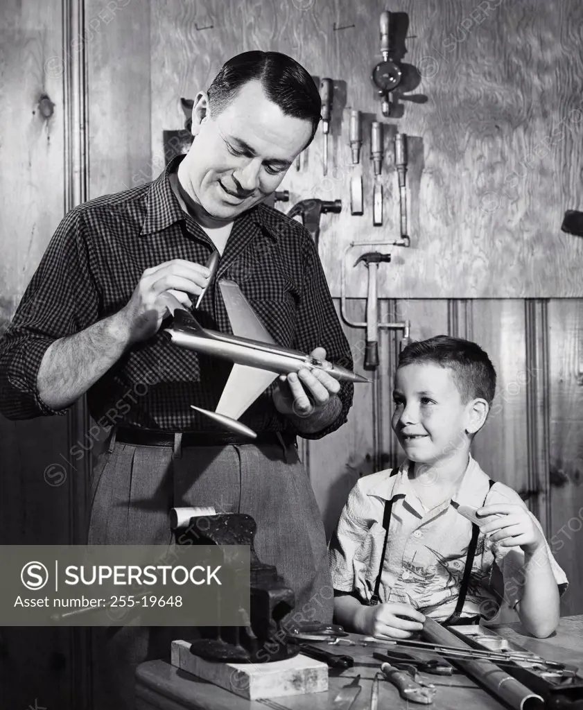 Father repairing a model airplane with his son standing beside him
