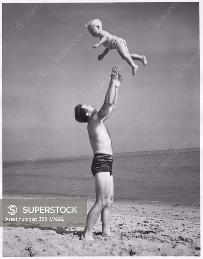 Side profile of a father tossing his son into the air at the beach
