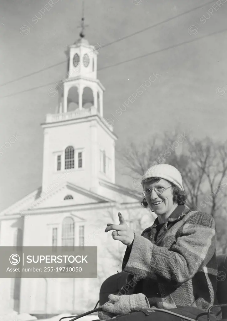 Vintage photograph. Woman pointing finger and smiling with white church in background