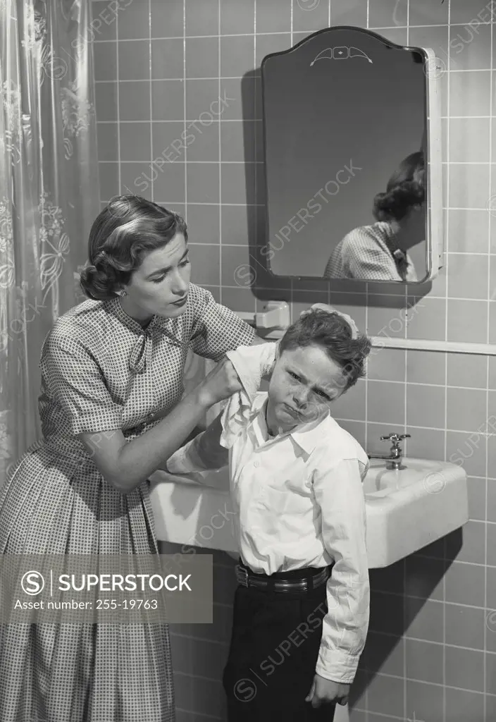 Mother cleaning unhappy young boys ear.