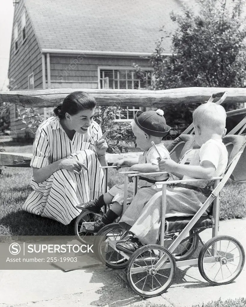 Close-up of a mother crouching with her two children sitting in baby strollers