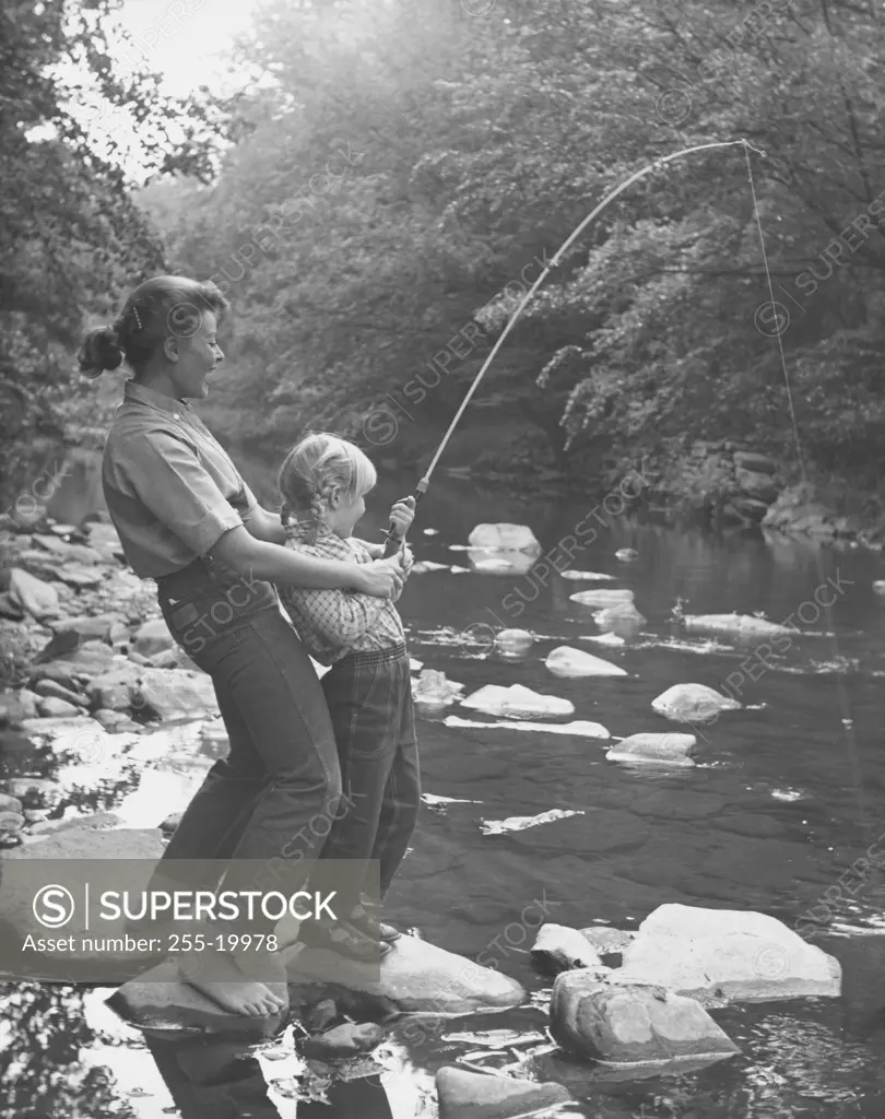 Mid adult woman with her daughter fishing in a stream