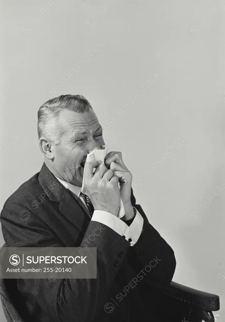 Vintage Photograph. Man wearing suit sitting in chair viewed from waist up sneezing, Frame 2