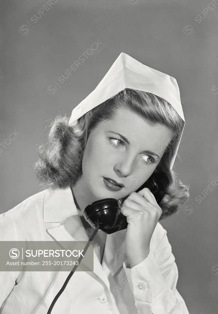 Vintage photograph. Smiling young blonde woman wearing white nurse uniform and cap talking on phone looking right