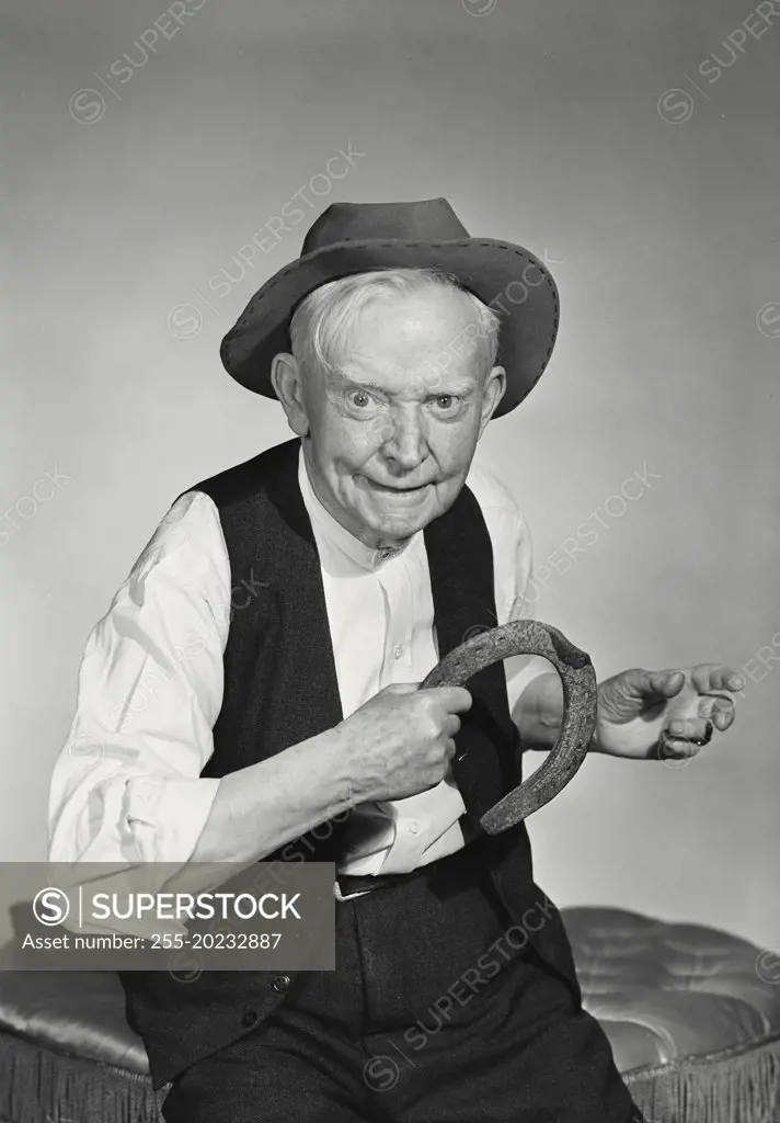 Prankster old man wearing hat and vest about to throw horseshoe