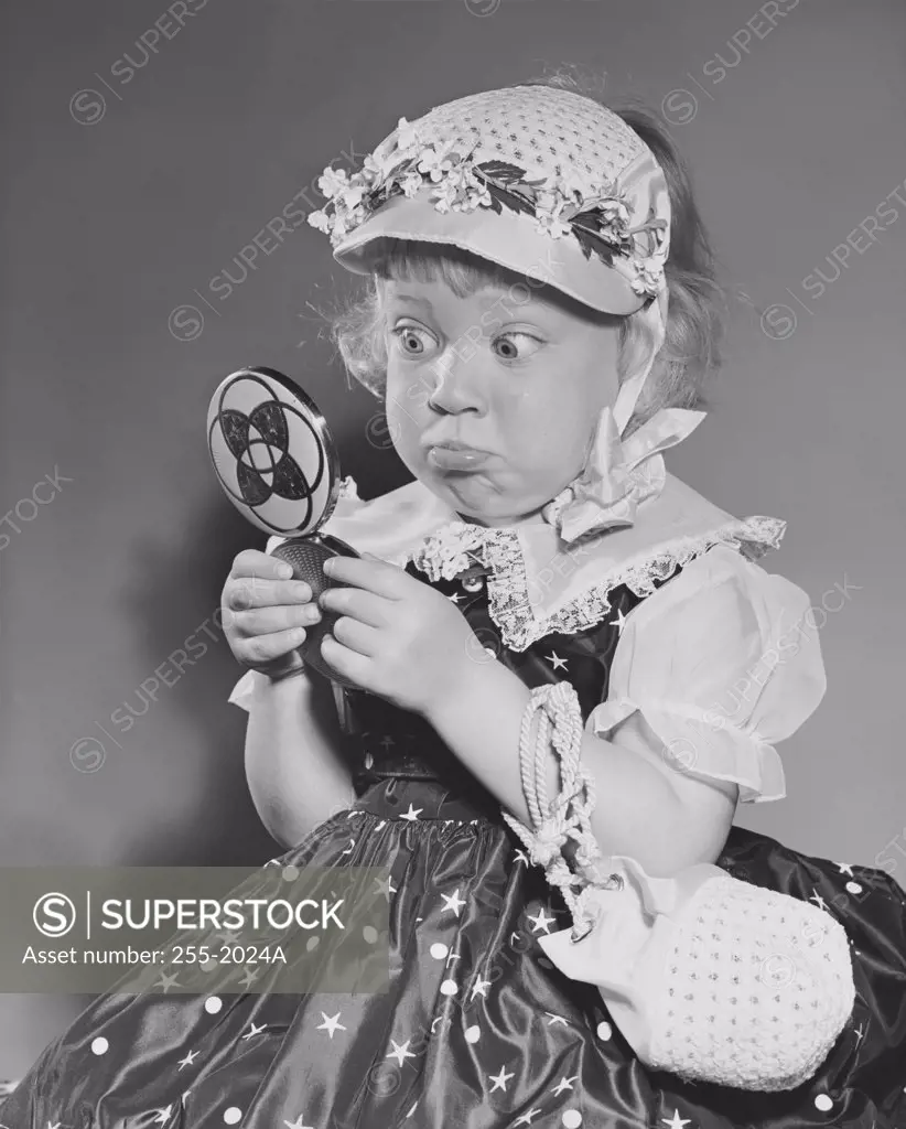 Close-up of a girl holding a hand mirror and making a face