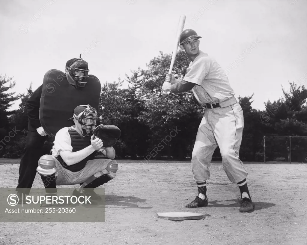 Baseball player swinging a baseball bat with a baseball catcher and a baseball umpire crouching beside him