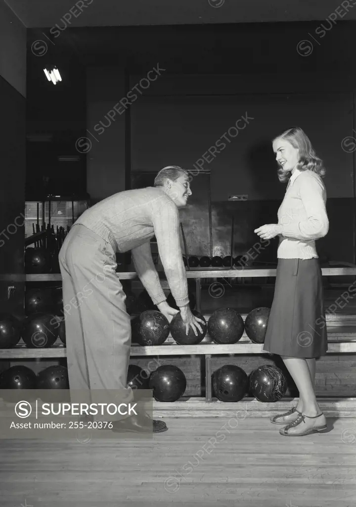 Vintage Photograph. Man grabbing bowling ball from shelf for a woman