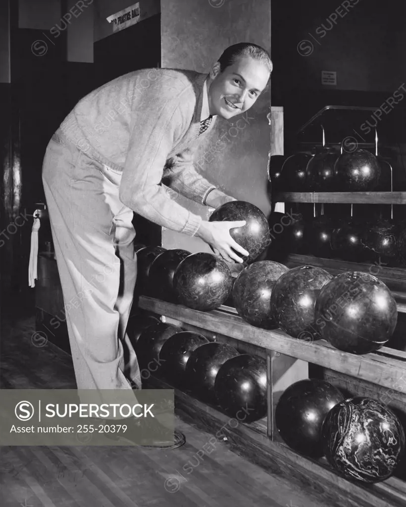Vintage Photograph. Young adult man reaching for bowling ball on shelf