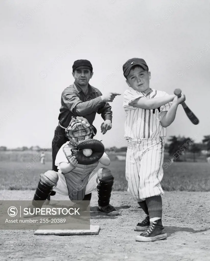 Two boys playing baseball with a baseball umpire standing behind them