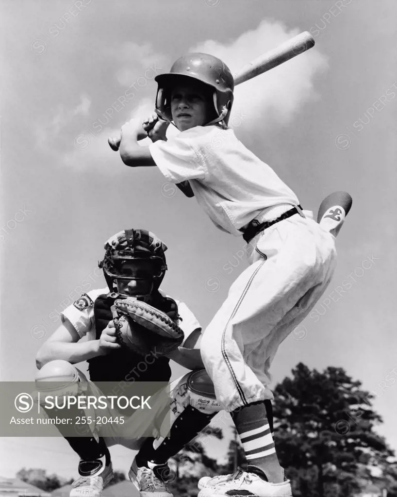 Youth league baseball player batting with a baseball catcher squatting behind him