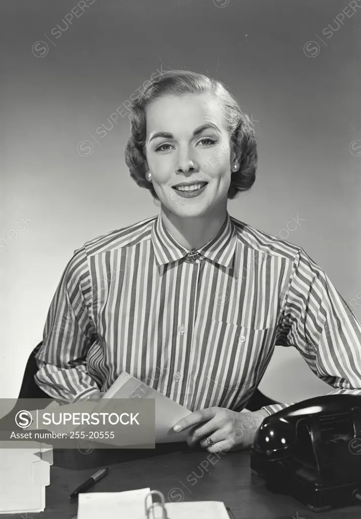 Vintage Photograph. Woman in striped collared blouse holding papers at desk and smiling