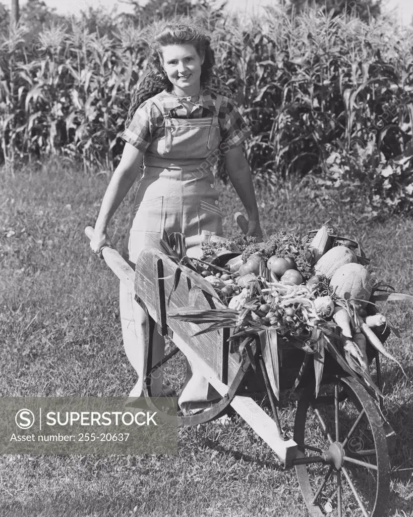 Young woman pushing a wheelbarrow with assorted vegetables in it