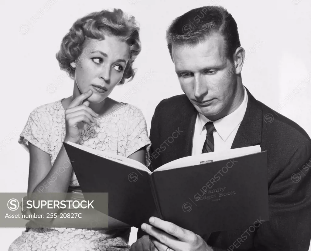 Close-up of a mid adult man reading a family budget book with a mid adult woman sitting beside him