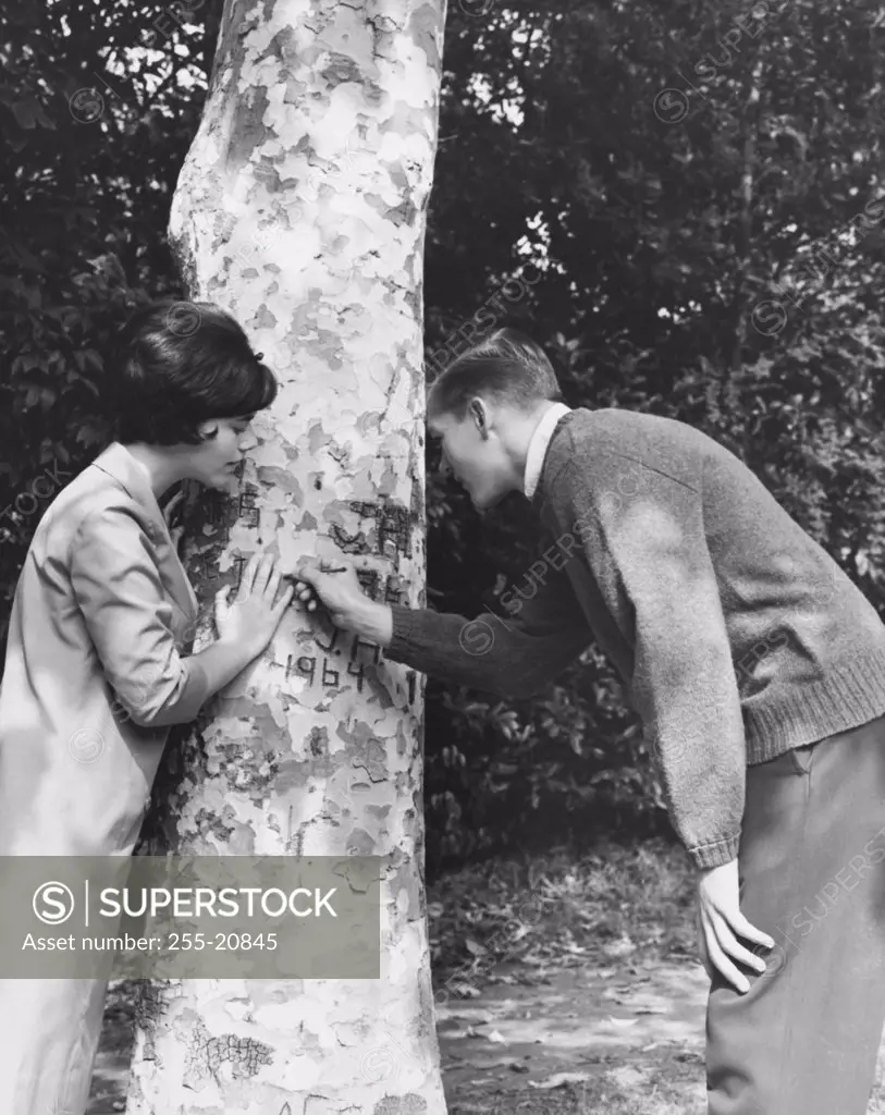 Side profile of a young couple carving their initials on a tree