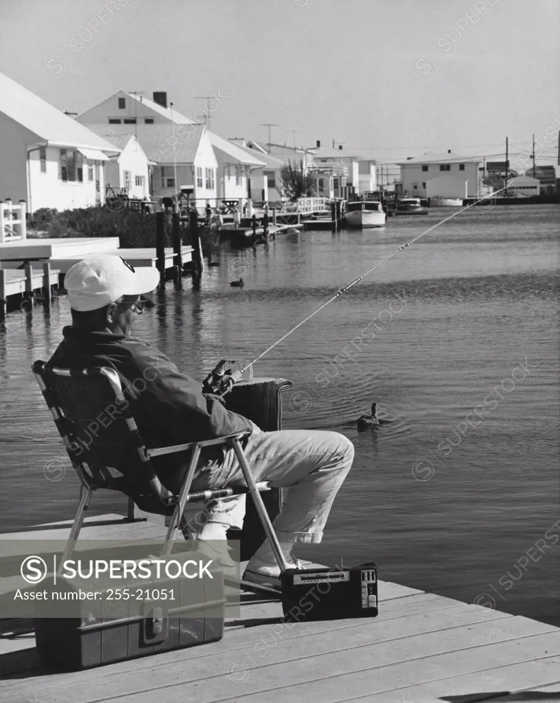 Mature man sitting in armchair and fishing in lake
