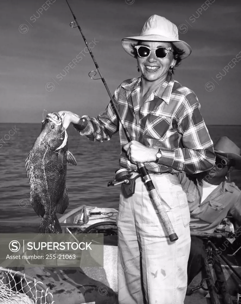 Mid adult woman holding a fish with a man sitting in the background