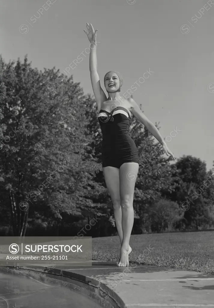 Vintage Photograph. Smiling woman wearing bathing suit and swim cap standing near edge of swimming pool outside with arm raised in air, Frame 2