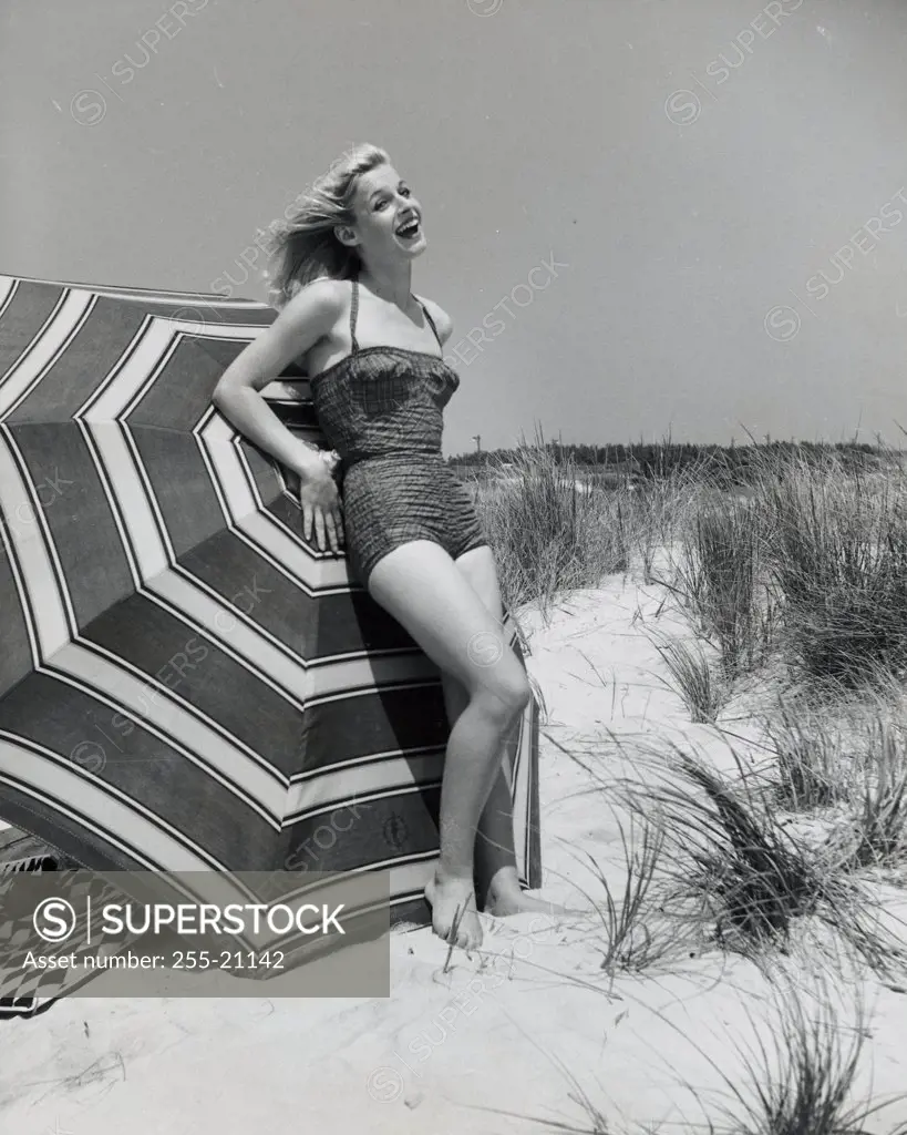 Side profile of a young woman leaning against a beach umbrella