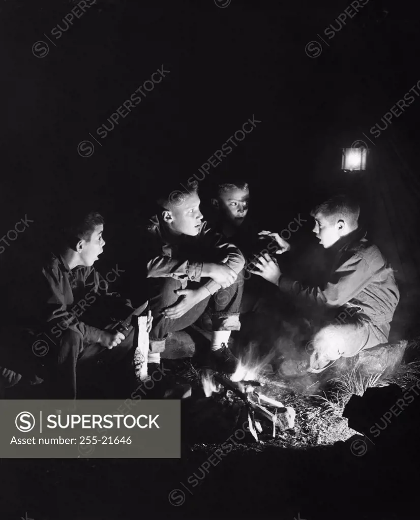 Boys listening to friend telling stories by campfire