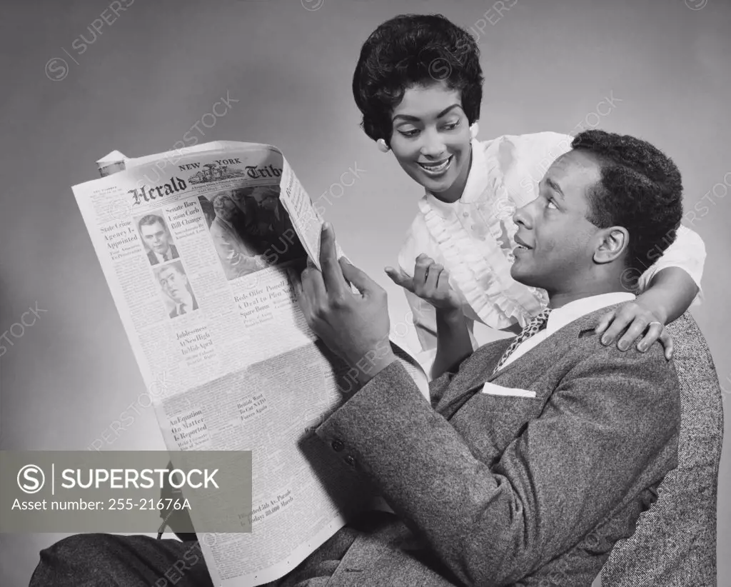 Side profile of a young man holding a newspaper with a young woman standing beside him