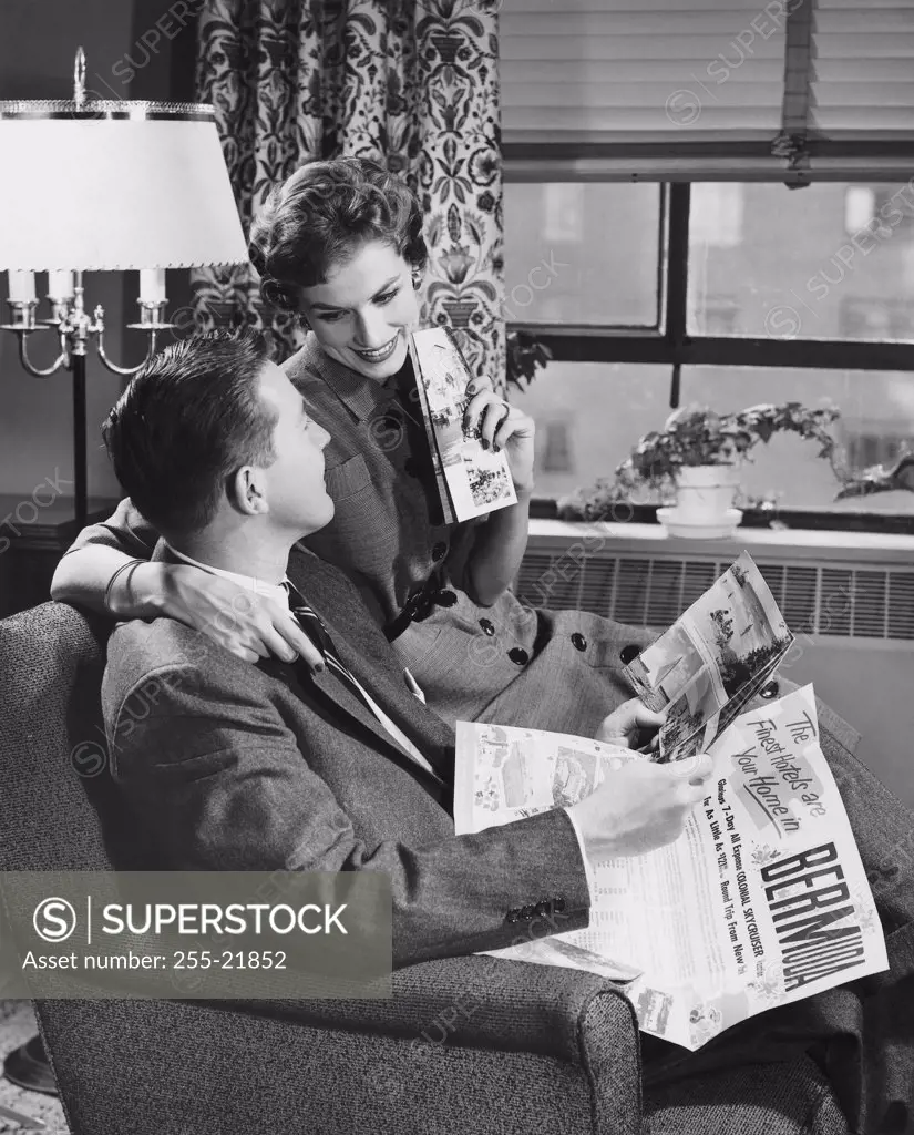 Side profile of young man holding vacation brochure with young woman sitting beside him