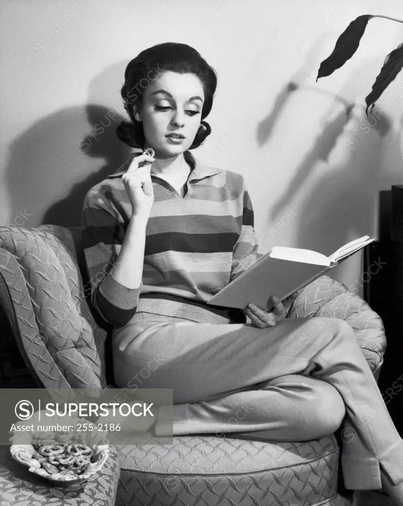Young woman reading a book and eating pretzels