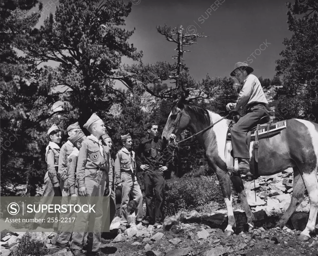 Side profile of a young man riding a horse in front of boy scouts at summer camp, Eldorado National Forest, California, USA