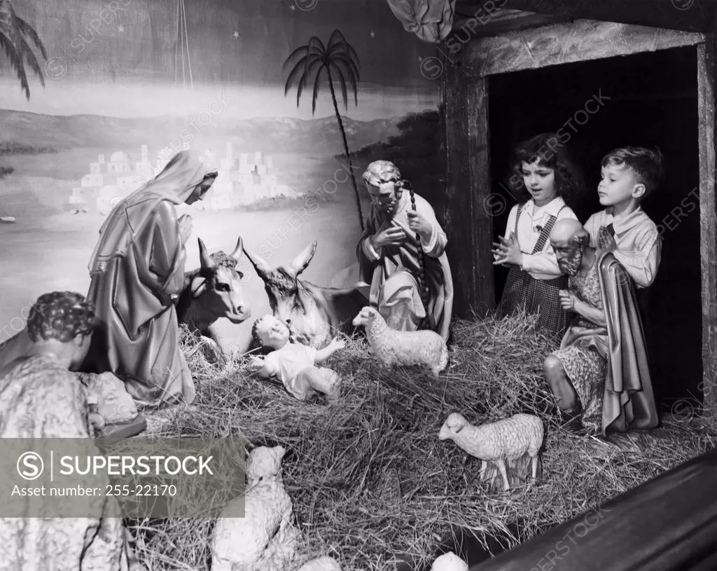 Boy and his sister standing near a Nativity scene