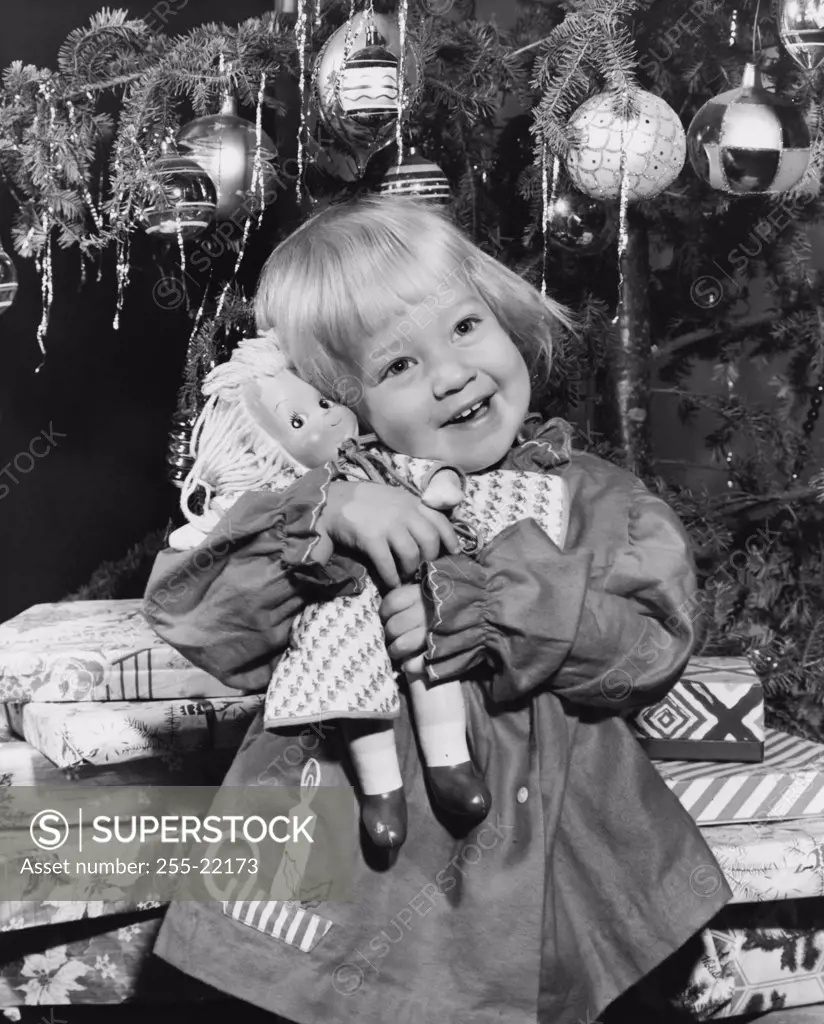 Close-up of a girl standing in front of Christmas presents and hugging a doll