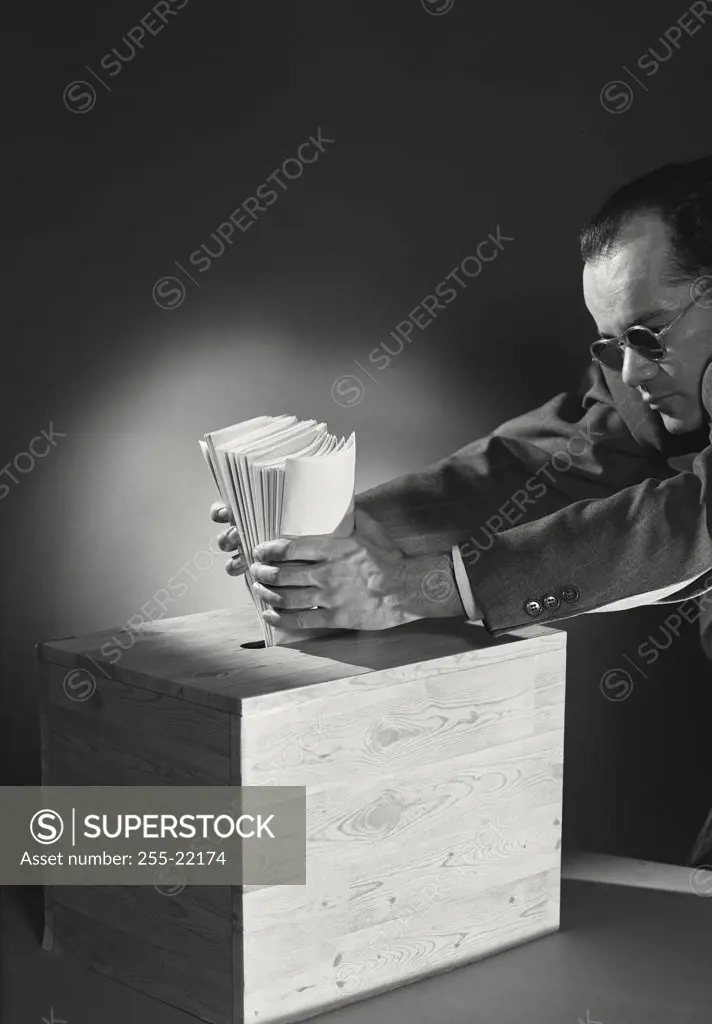 Vintage photograph. Man in sunglasses placing stack of folded ballots into slot of wooden box