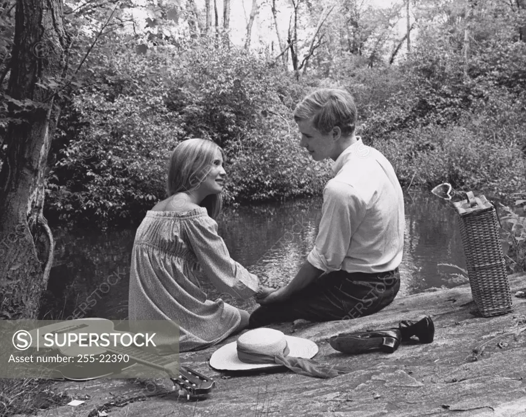 Rear view of a young couple sitting near a pond