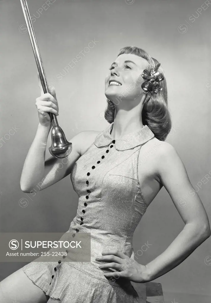 Vintage photograph. Young woman in dress and headband holding baton smiling looking up