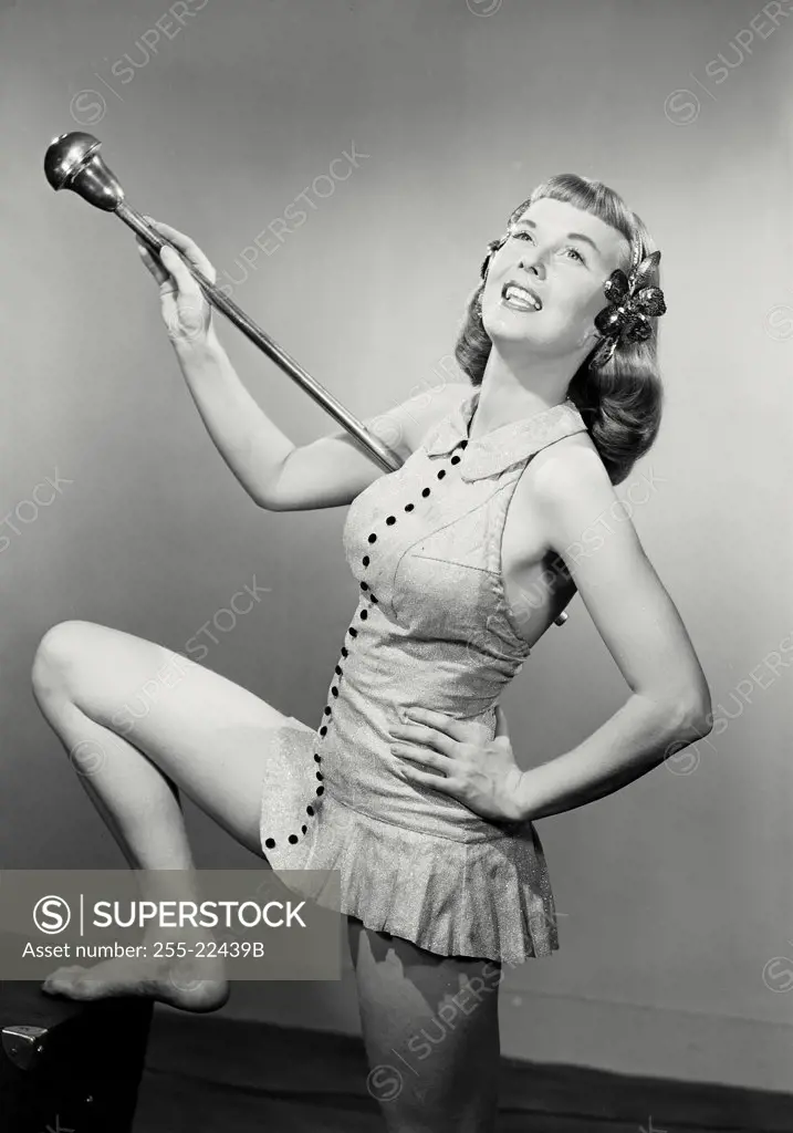 Vintage photograph. Young woman in dress and headband holding baton with knee up