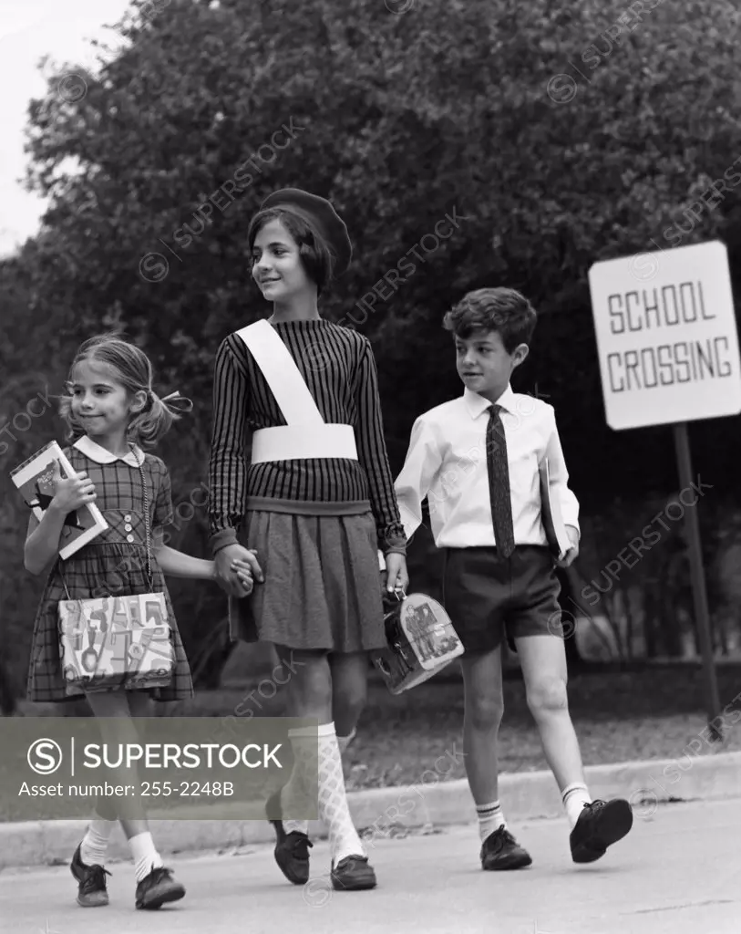 Female crossing guard assisting a boy and girl at road crossing
