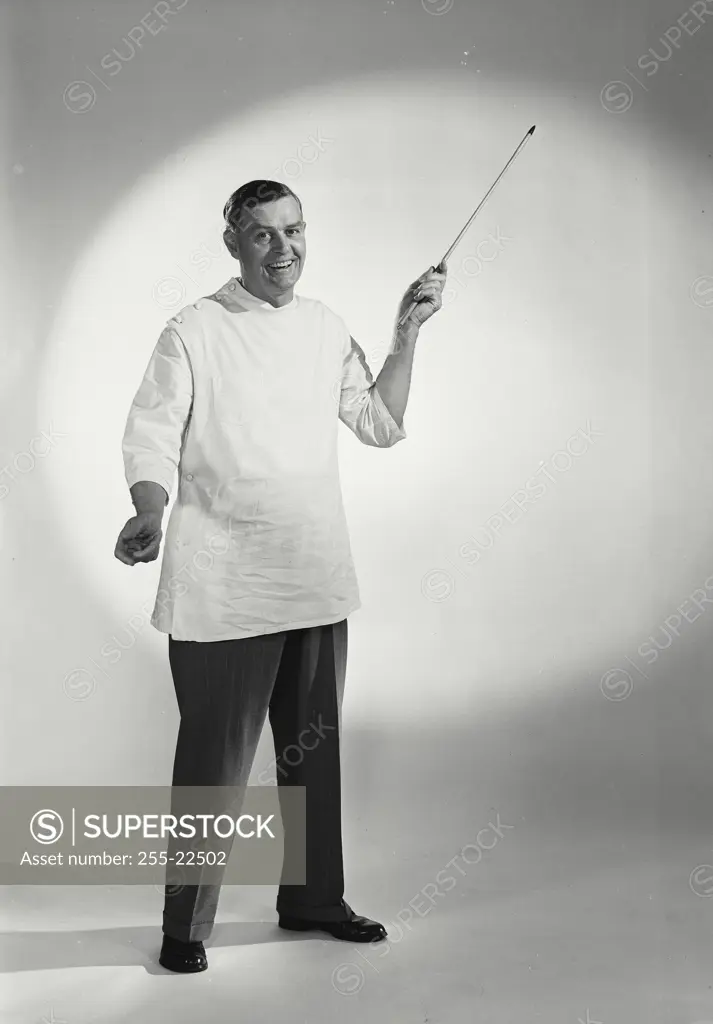 Vintage Photograph. Smiling man wearing doctor's smock holding wooden presentation pointer up in front of white background