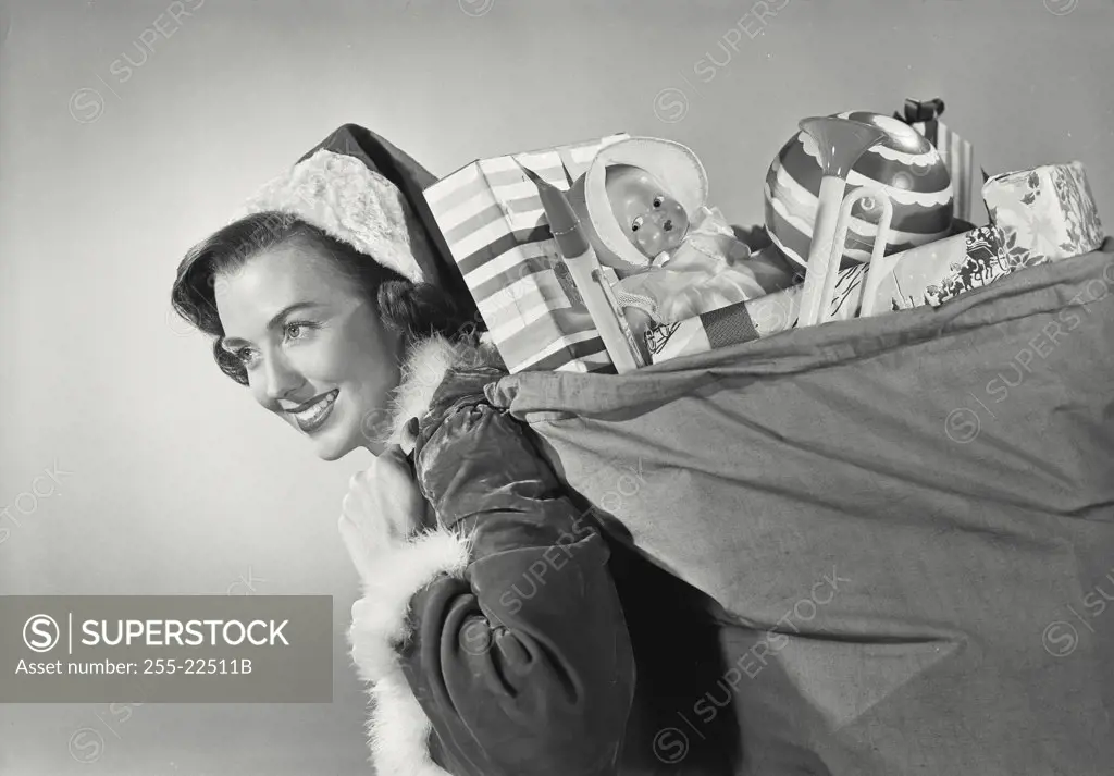 Vintage photograph. Close-up of a brunette woman in Santa Claus hat smiling carrying sack full of childrens toys