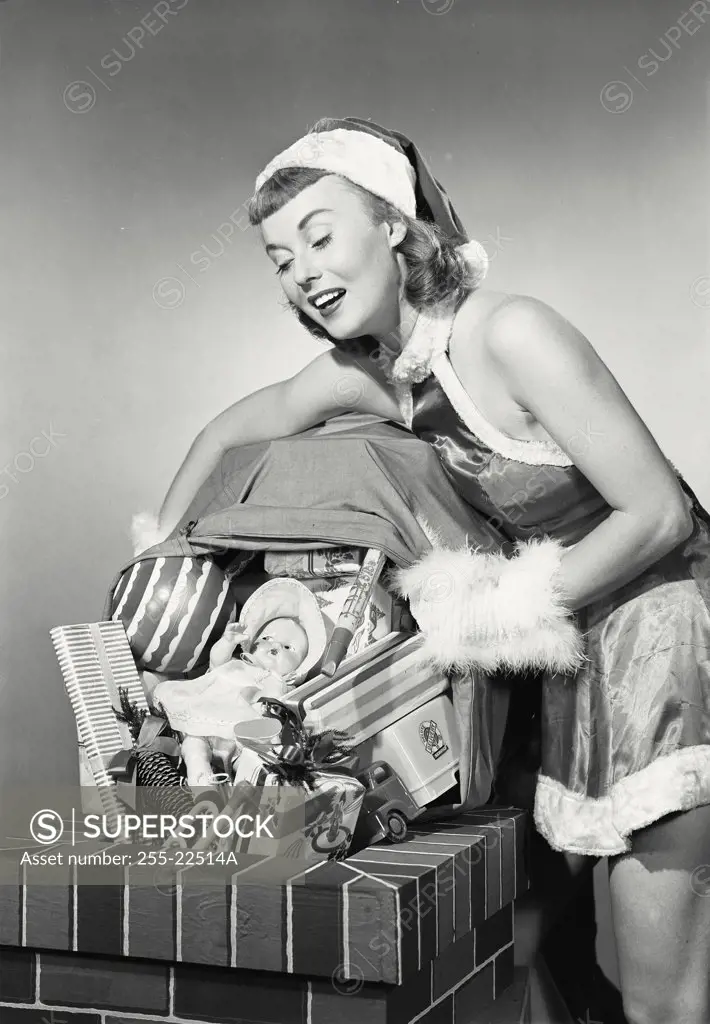 Vintage photograph. Close-up of a young woman dressed as santa dumping toys down chimney
