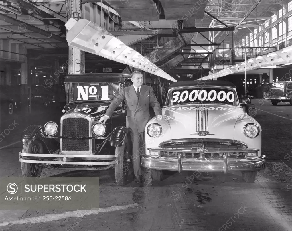 Mature man standing with first and 3 Millionth Pontiac, March 1949