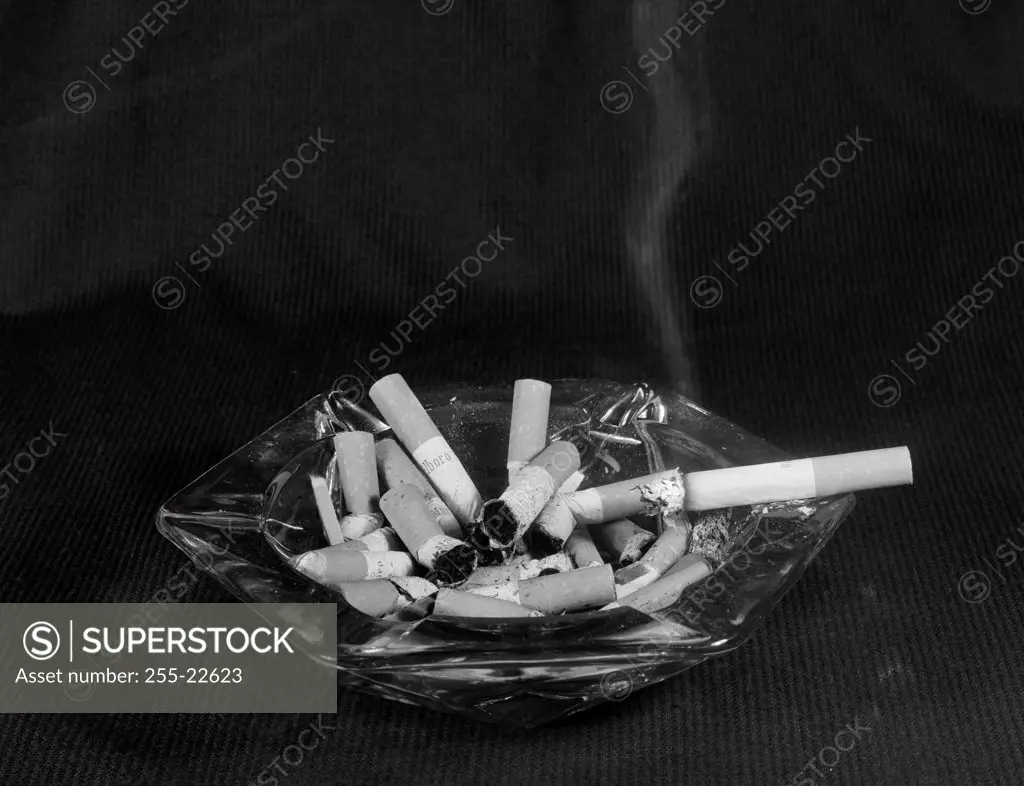 Ashtray full of cigarette butts with single cigarette smoking
