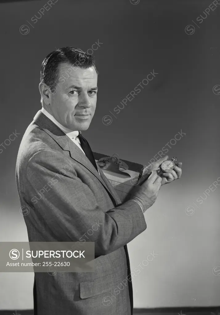 Vintage Photograph. Man in suit holding clipboard and stopwatch looking at camera
