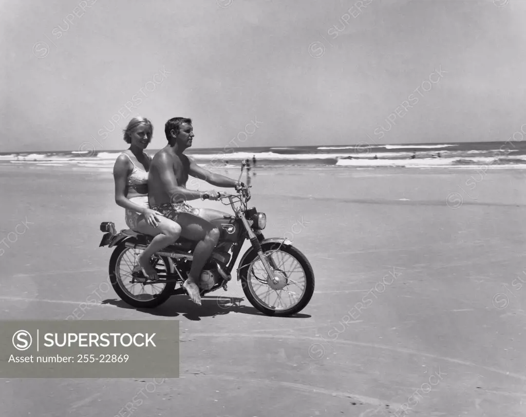 Young couple riding motorcycle on beach